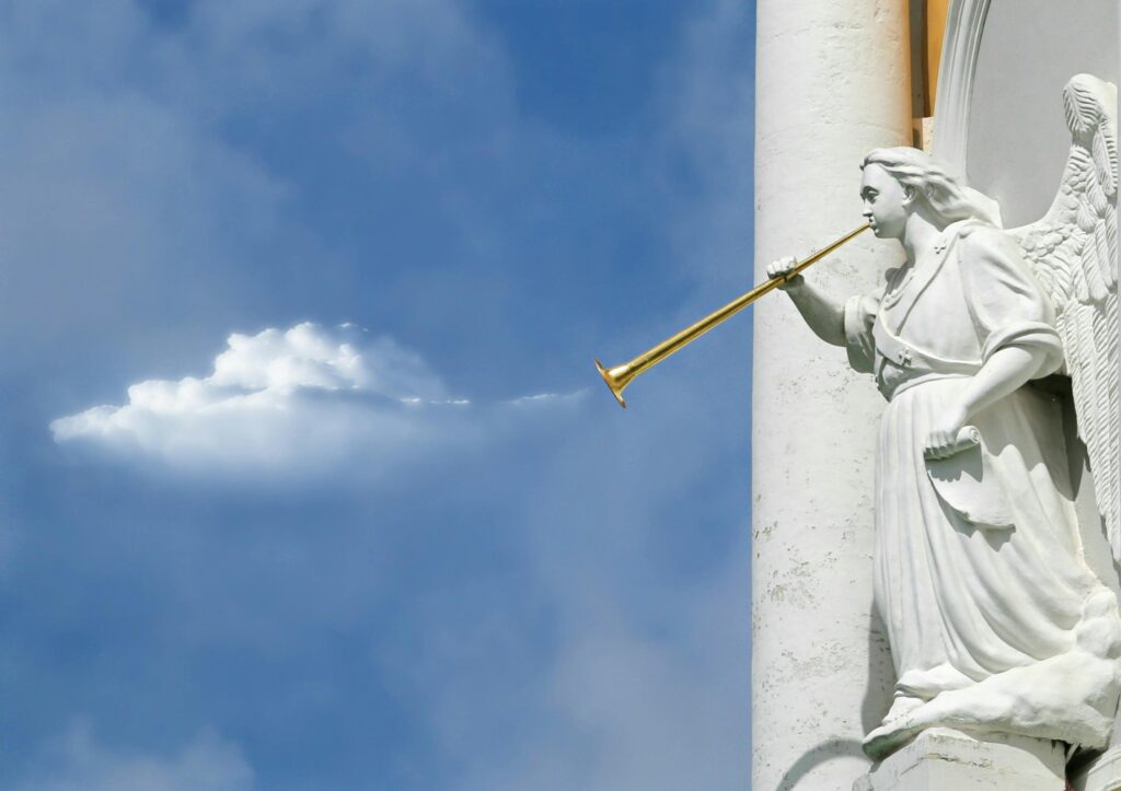 Sculpture of an angel with a trumpet, set against a bright blue sky with clouds.