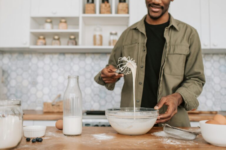 Man in kitchen mixing batter with ingredients like milk and blueberries, creating a cozy preparation scene.