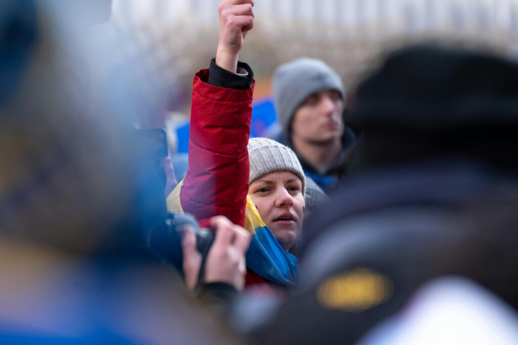 A woman in a red jacket raises her fist at a protest in New York City, symbolizing solidarity.