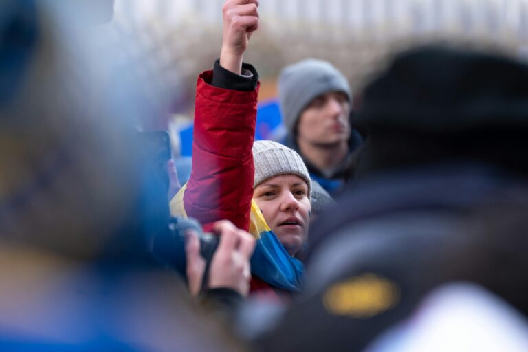 A woman in a red jacket raises her fist at a protest in New York City, symbolizing solidarity.