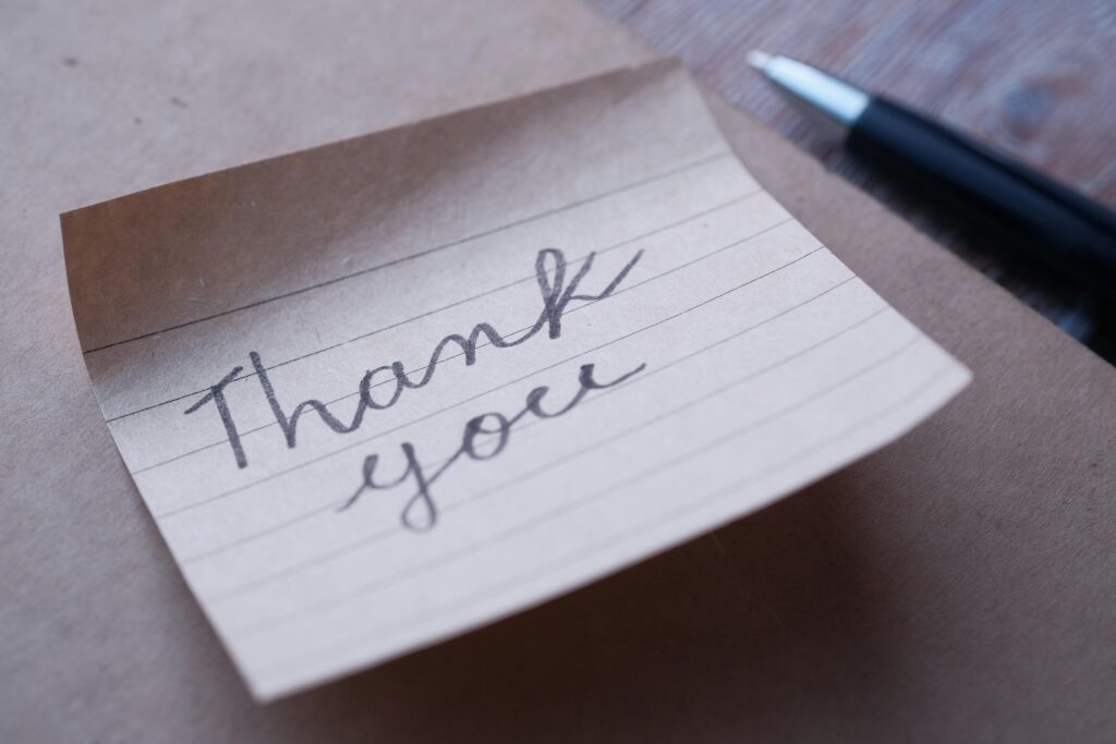 Close-up of a handwritten thank you note on brown paper with a pen nearby.