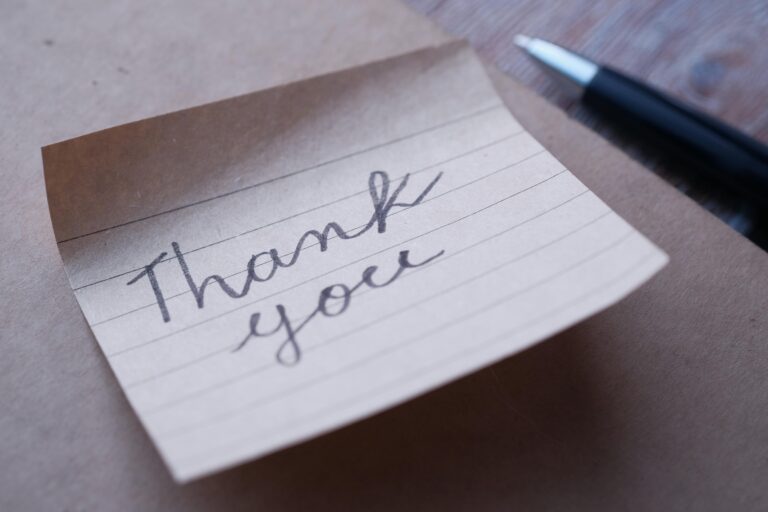 Close-up of a handwritten thank you note on brown paper with a pen nearby.